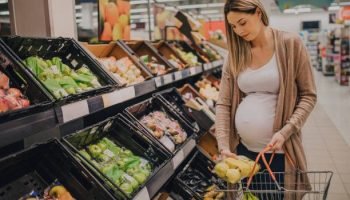 A young pregnant woman is grocery shopping in a supermarket store.