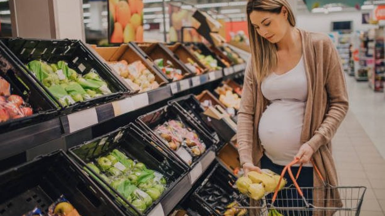 A young pregnant woman is grocery shopping in a supermarket store.