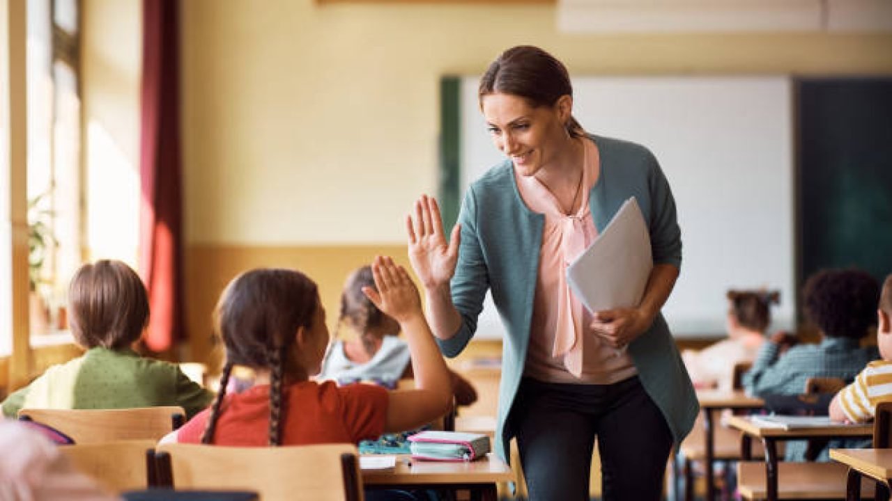 Happy elementary school teacher giving high-five to her student during class in the classroom.