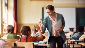 Happy elementary school teacher giving high-five to her student during class in the classroom.