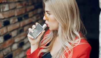 Stylish girl in a city. Lady use the electronic cigarette. Woman in a red jacket.