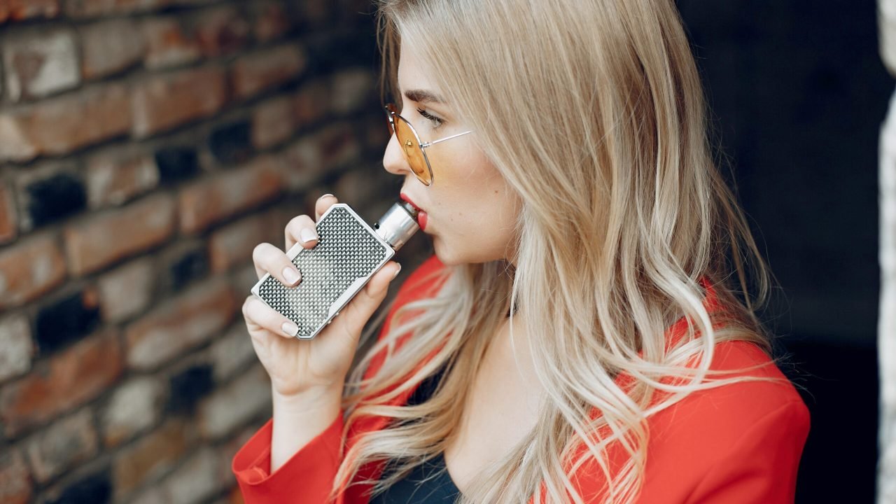 Stylish girl in a city. Lady use the electronic cigarette. Woman in a red jacket.